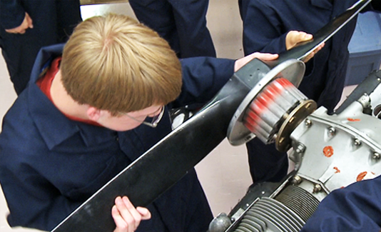 A picture of a young man with a group of other students fitting in a propeller. 